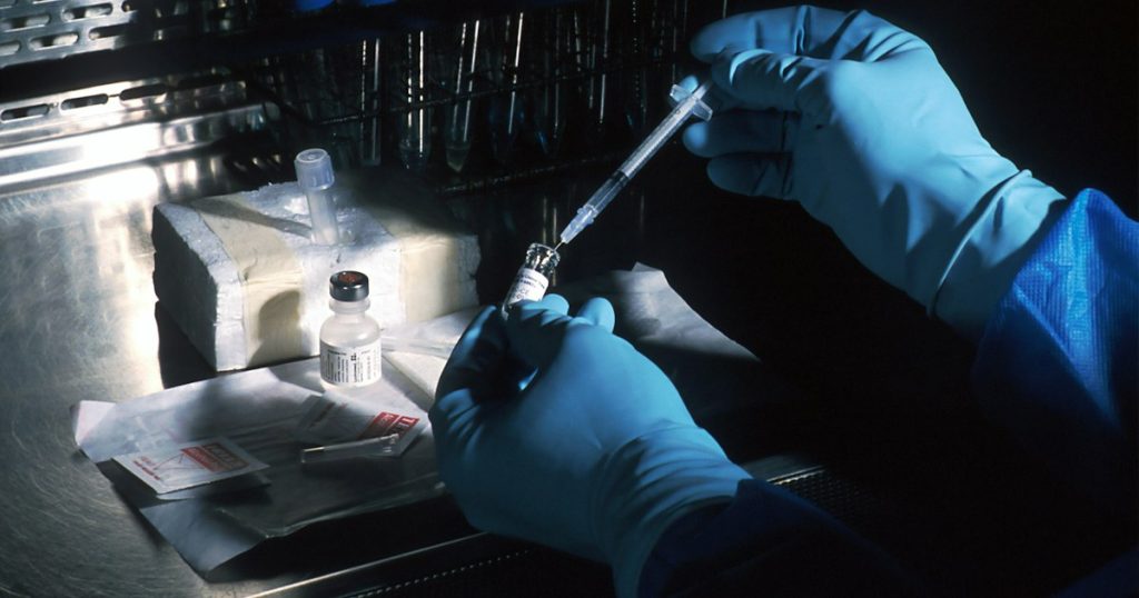 Gloved hands drawing medication from a vial into a syringe