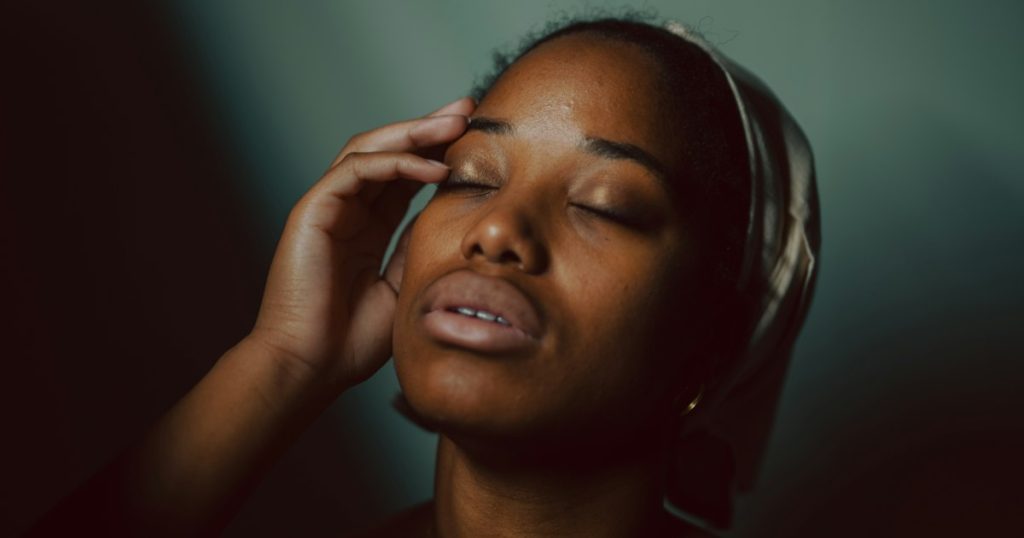 Woman resting with her eyes closed and a hand to her temple in a softly lit room
